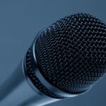 A detailed close-up of a microphone with a blue monochrome background, highlighting its intricate mesh design.